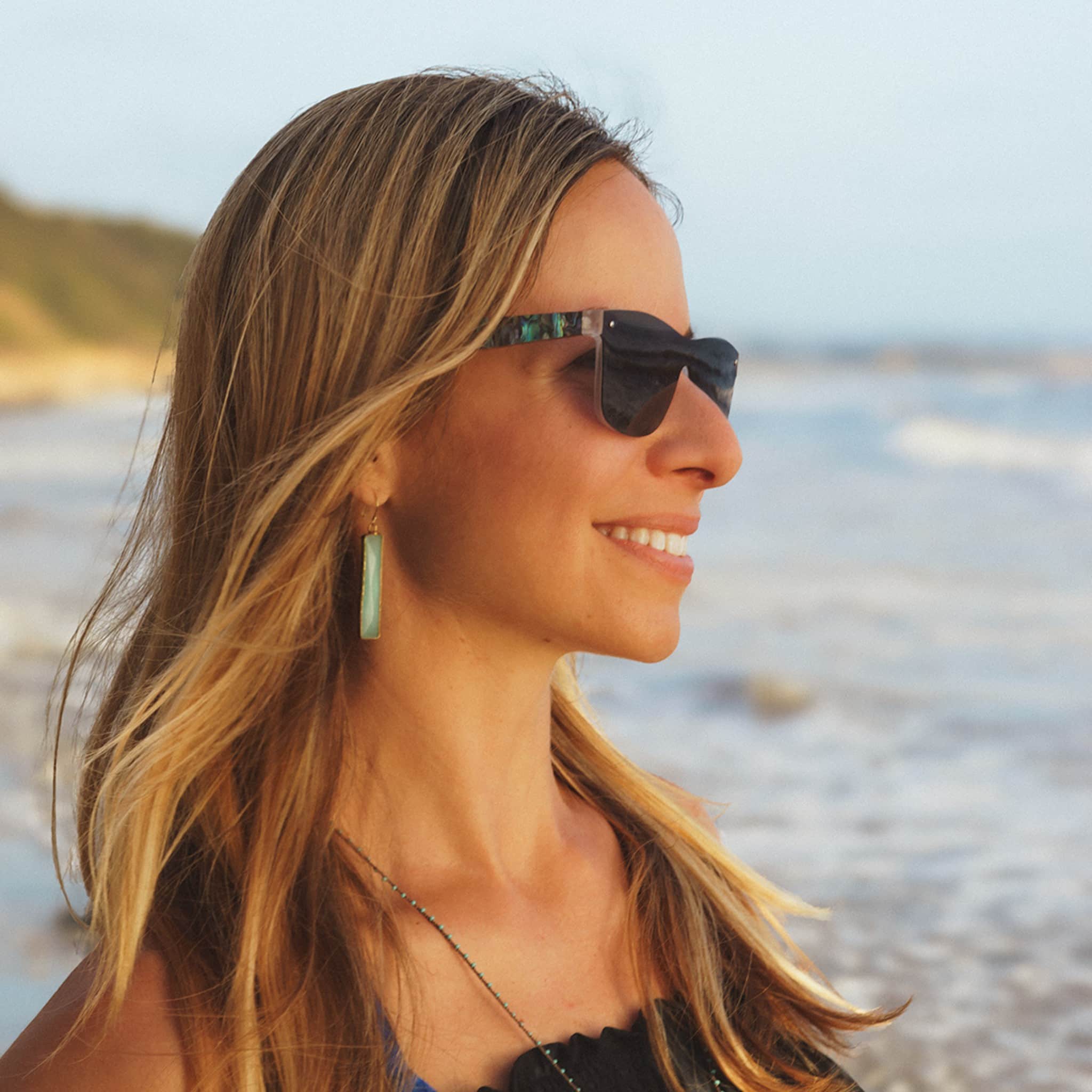 Blonde female model wearing Soul California Eyewear Maui sunglasses crafted from Abalone Seashell, Zebra Wood, and rPC with polarized light black lenses.