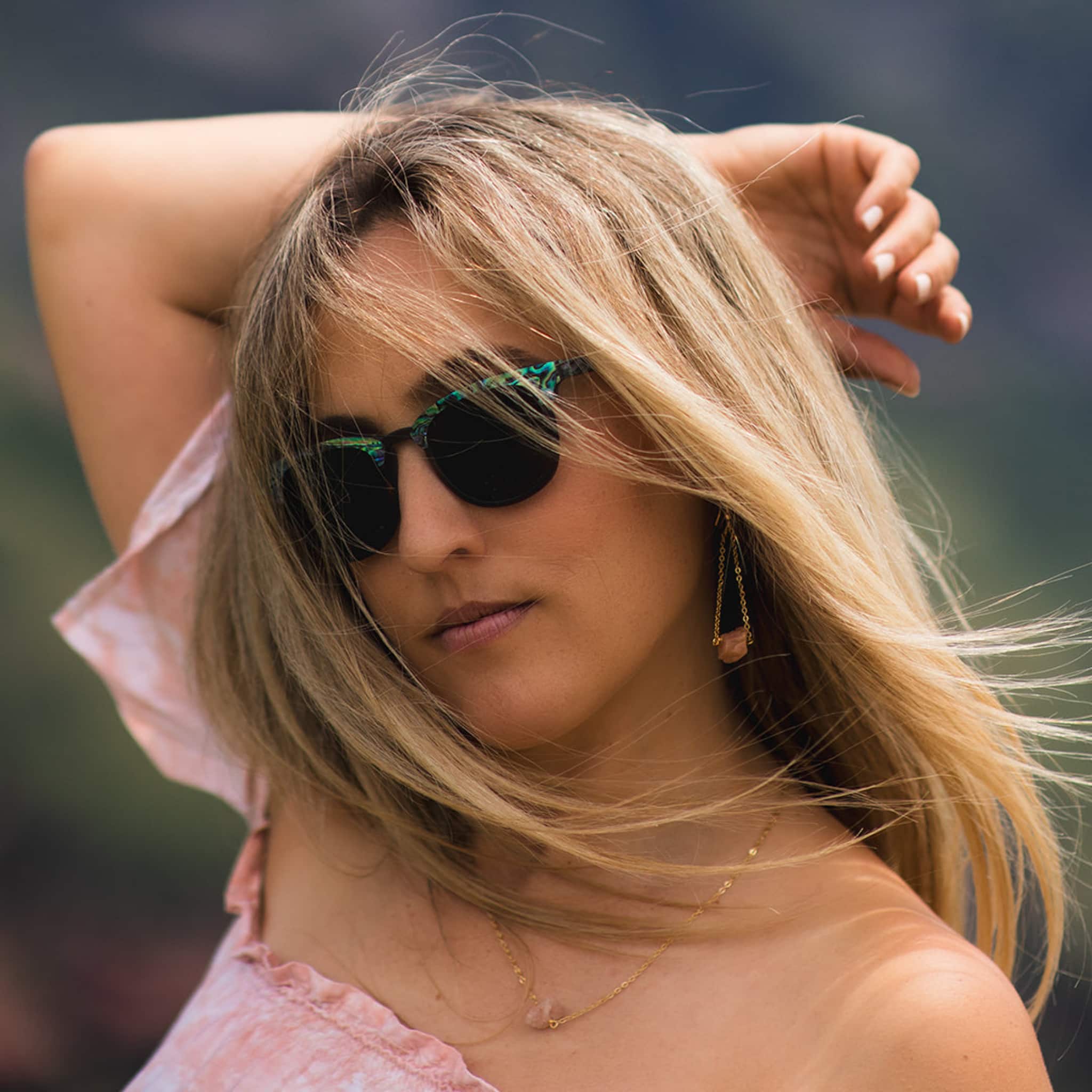Blonde female model wearing Soul California Eyewear Pebble Beach Dusk 2 sunglasses handcrafted from ebony wood and genuine abalone shell with polarized black lenses.