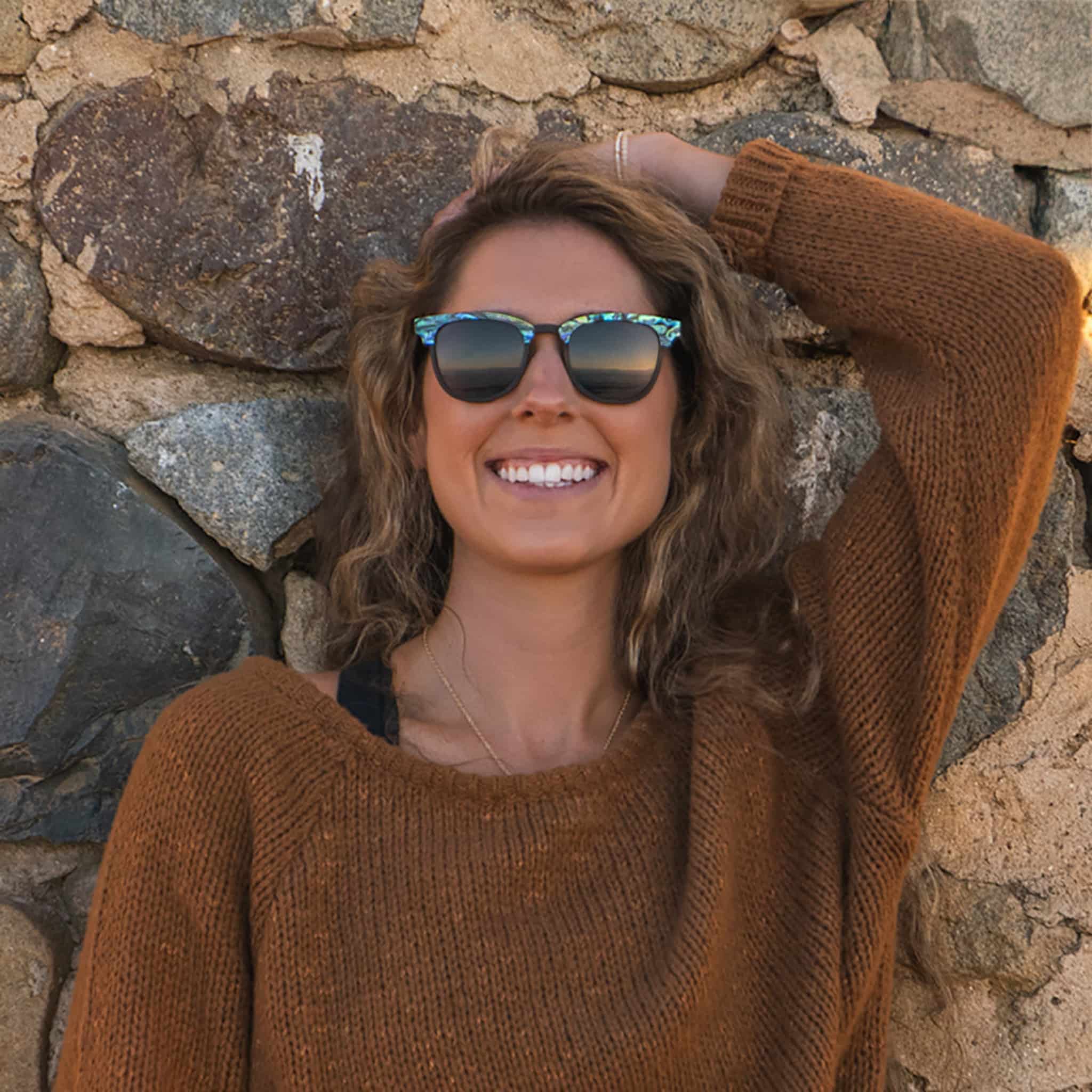 Brunette female model wearing Soul California Eyewear Pebble Beach Dusk 2 sunglasses crafted from ebony wood and genuine abalone shell with polarized black lenses.