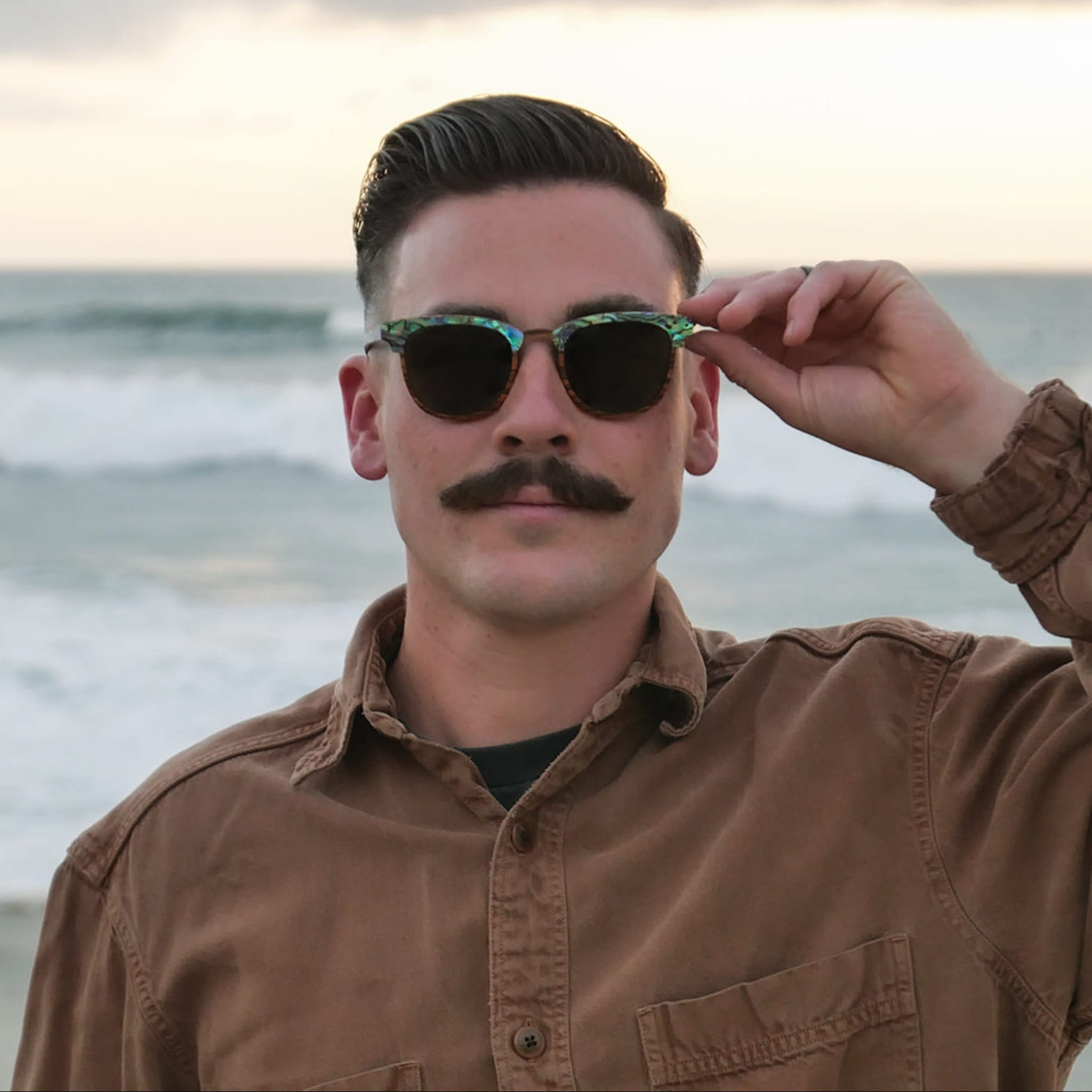 Male model wearing Soul California Eyewear Pebble Beach Dusk sunglasses handcrafted from zebra wood and genuine abalone shell with polarized light black lenses.