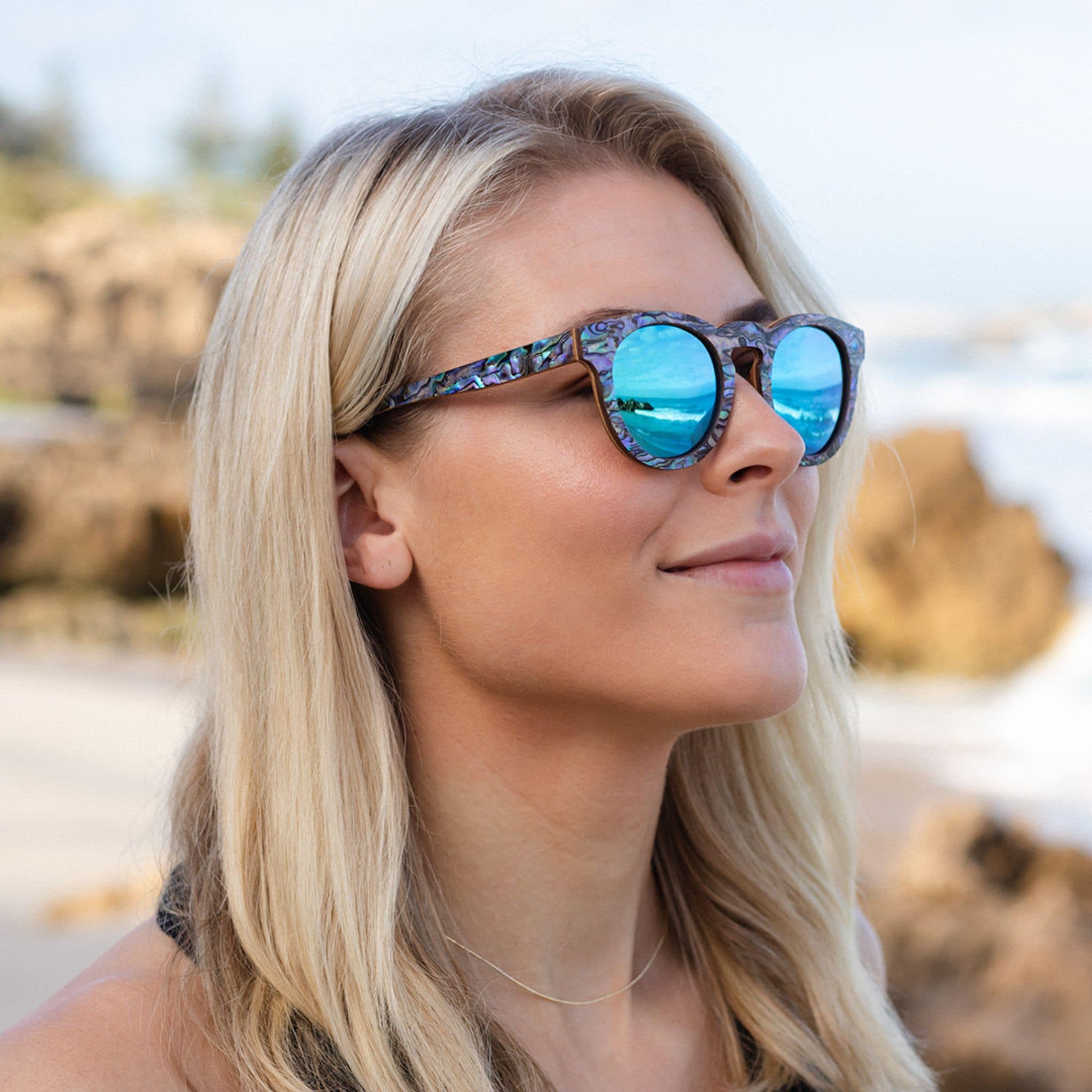 Model wearing Soul California Eyewear Pfeiffer Beach sunglasses handcrafted from Zebra Wood & New Zealand Abalone Paua Shell with polarized blue lenses.